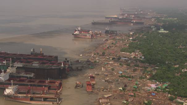 Carcasses of dismantled boats on the seafront, workers at work